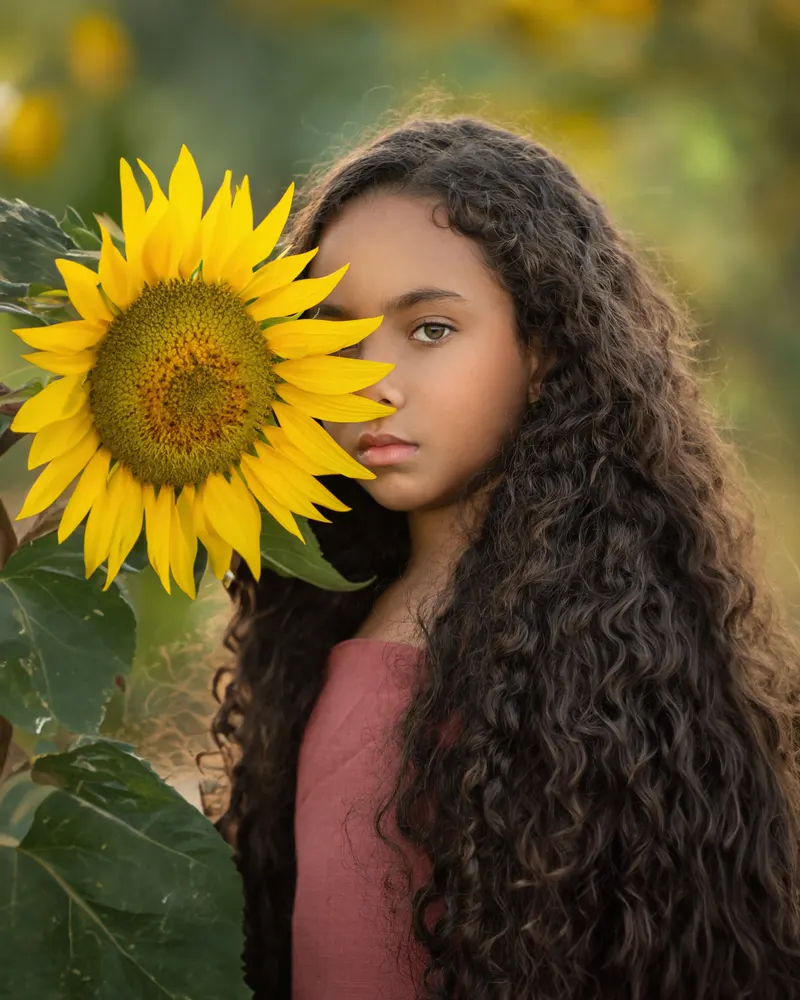 Niña de cabello rizado junto a un girasol
