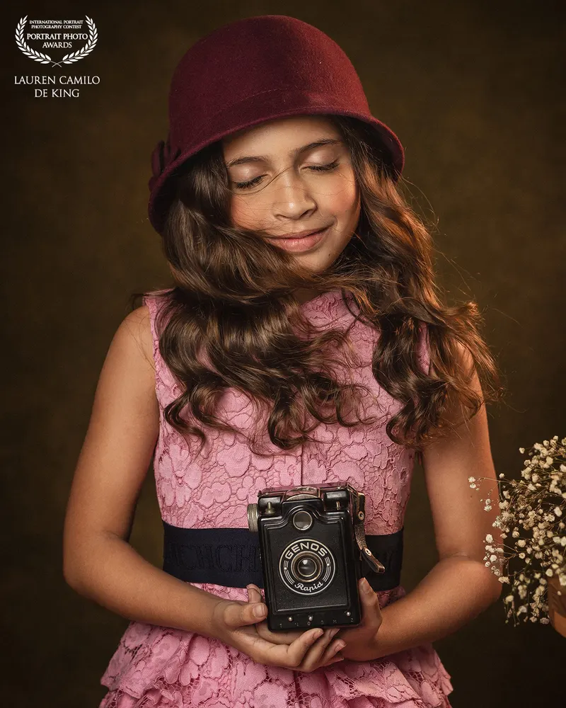 Niña con sombrero rosado sosteniendo una cámara antigua