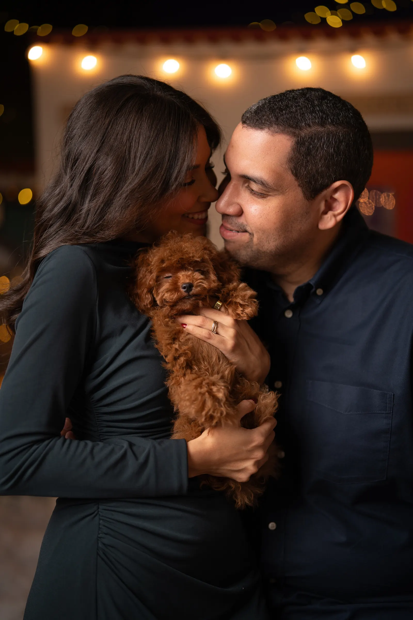 Pareja abrazando a su perrito entre luces navideñas